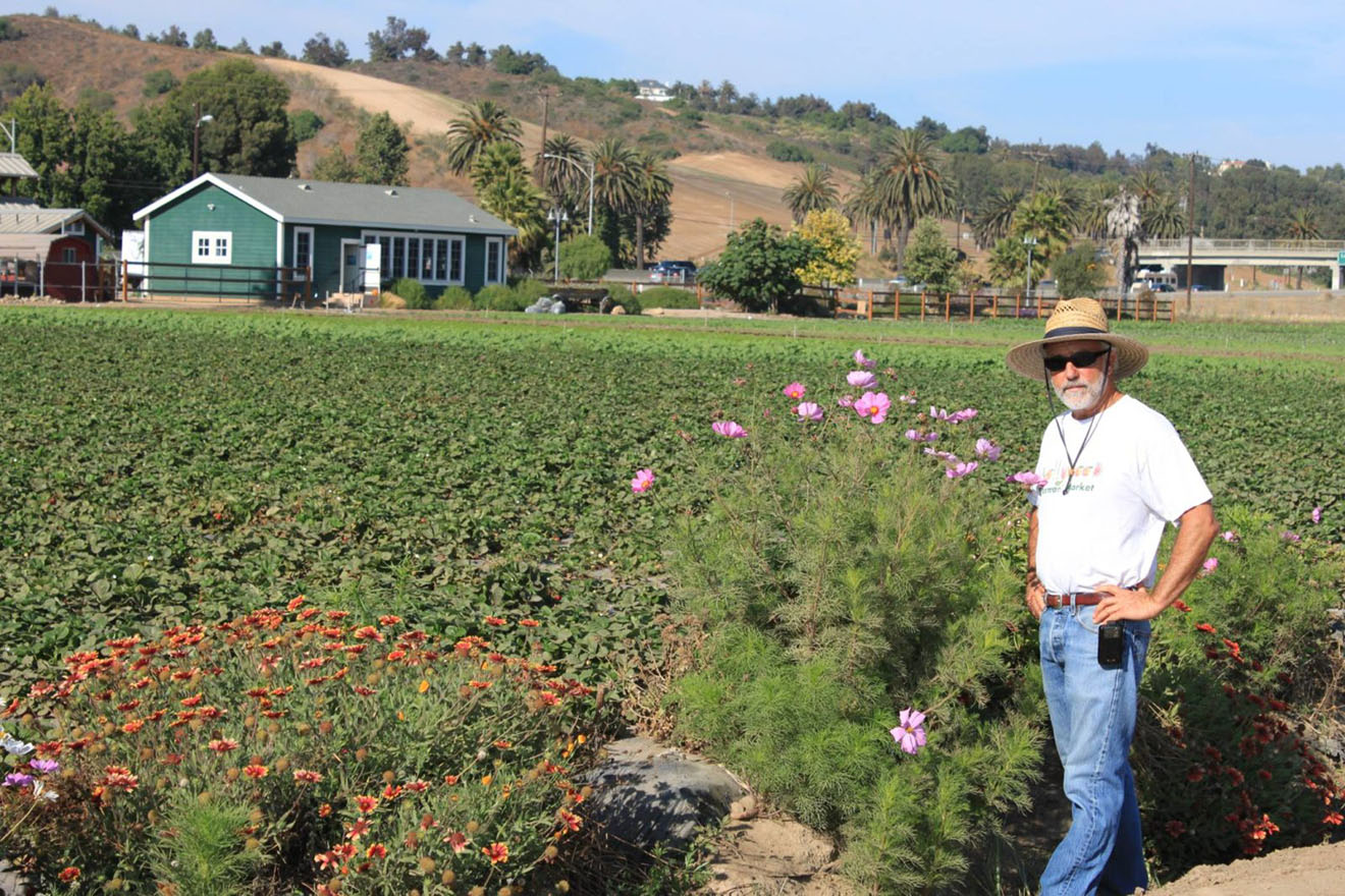 Farmer standing in front of his field with a house in the background