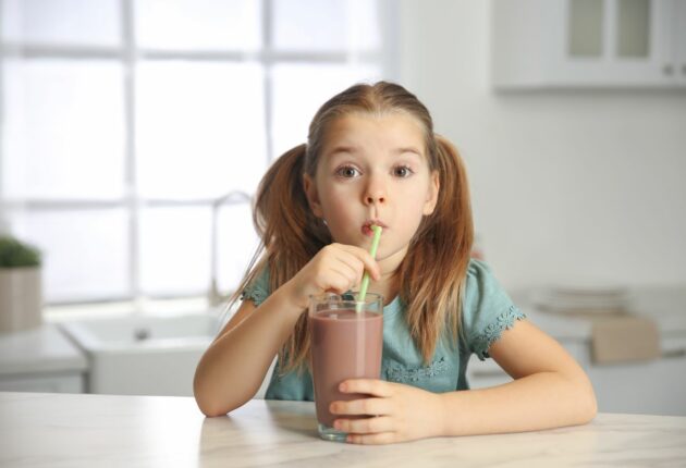A little girl drinking from a glass of chocolate milk with a straw